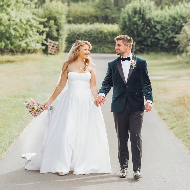 Wedding couple walking hand in hand on a path with greenery in the background with a dried flower bouquet from the happy blossoms